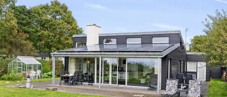 A modern house with a glass conservatory, a patio with outdoor furniture, and a solar panel roof.