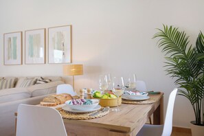 A dining table set with plates, glasses, and bread, surrounded by white chairs and a sofa.