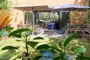 Un patio con mobiliario exterior, cerramiento de vidrio y vista al interior.