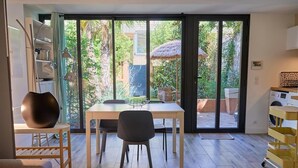 Ein modernes Zimmer mit Esstisch, Stühlen, einer Couch, einem großen Fenster und einer Schiebetür, die zu einem Garten führt.
