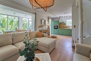 A living room with a sofa, a dining area with a table, and a kitchen with green cabinets.