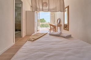 A bedroom with a bed, a desk, a chair, a mirror, and a balcony with a view.
