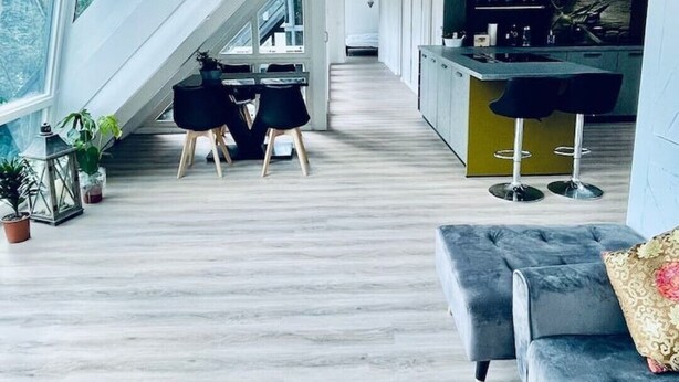Un moderno espacio tipo loft con techo alto, tragaluces, zona de cocina y área de estar con sofá y sillones.
