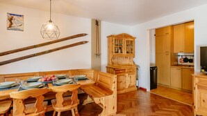A wooden dining area with a bench, a wooden cabinet, and a kitchen area with wooden cabinets and a stove. - Enrosadira by Interhome (Canazei)