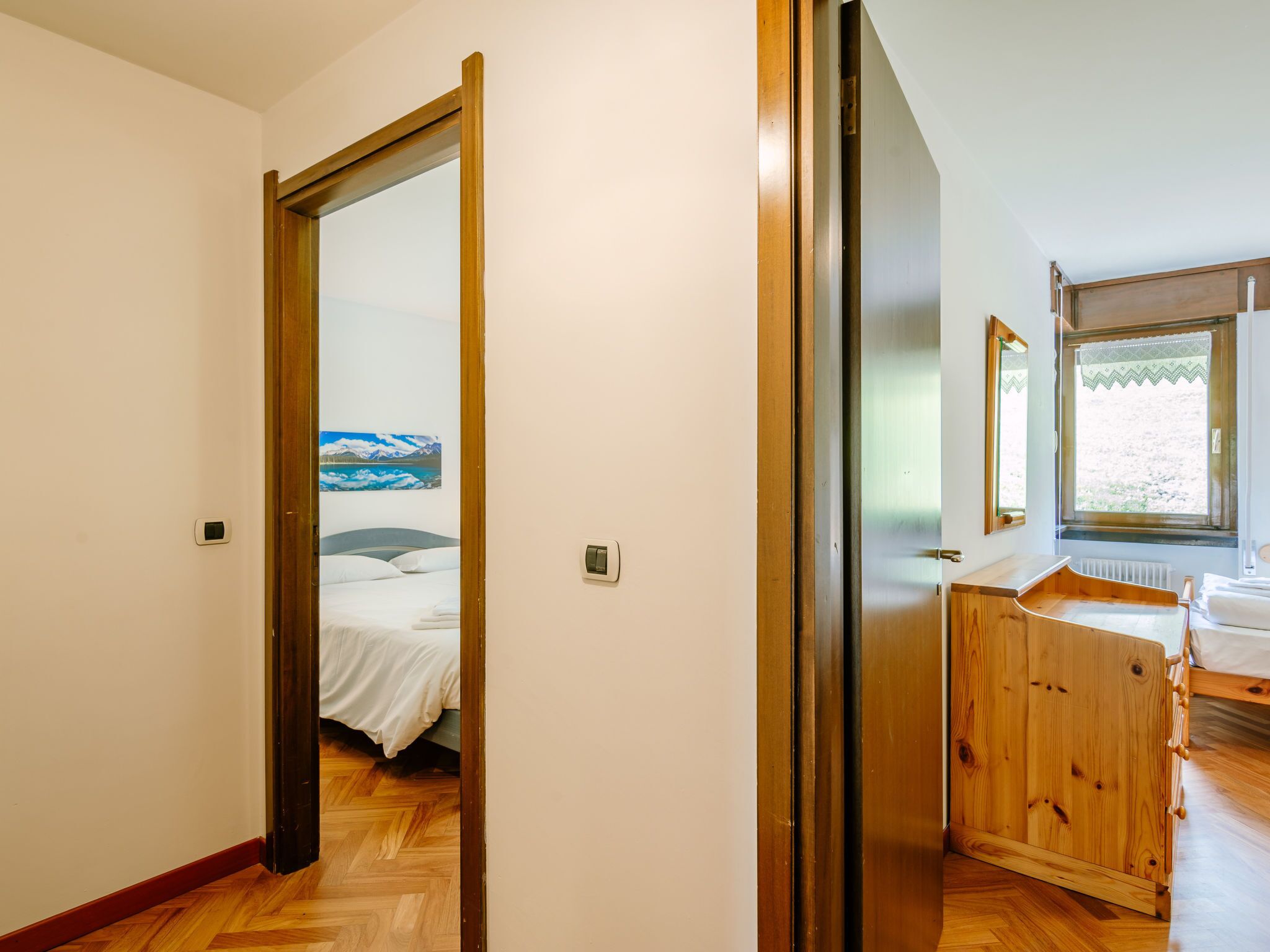 A bedroom with a wooden wardrobe, a bed with white bedding, and a window with a view of the outdoors.