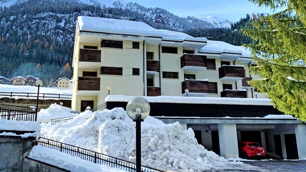 A multi-story building with a snow-covered roof, surrounded by snow and trees. - Enrosadira by Interhome (Canazei)