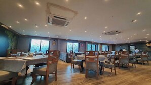 A restaurant with multiple tables and chairs, large windows, and an air conditioning unit on the ceiling.