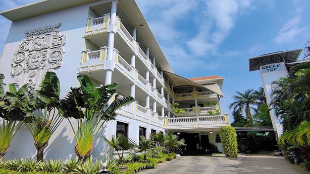 A multi-story hotel with a white facade, balconies, and tropical landscaping.