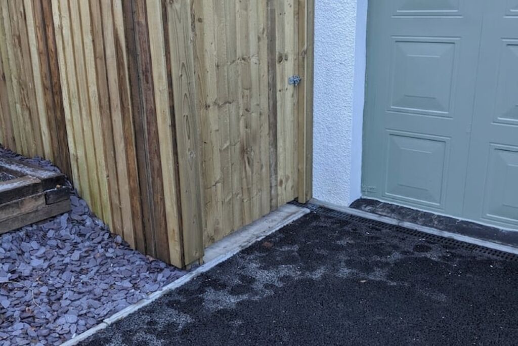A wooden gate leading to a driveway with a gravel path and a green door.