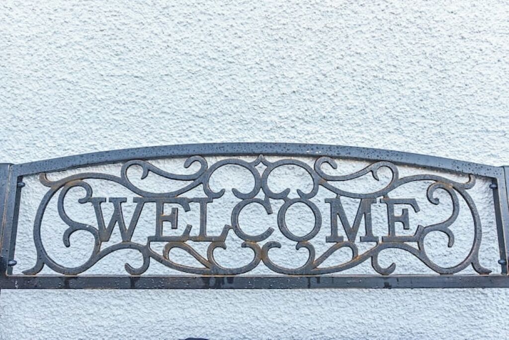 Een metalen bord met de tekst 'WELCOME' in sierlijke letters voor een gestructureerde muur.