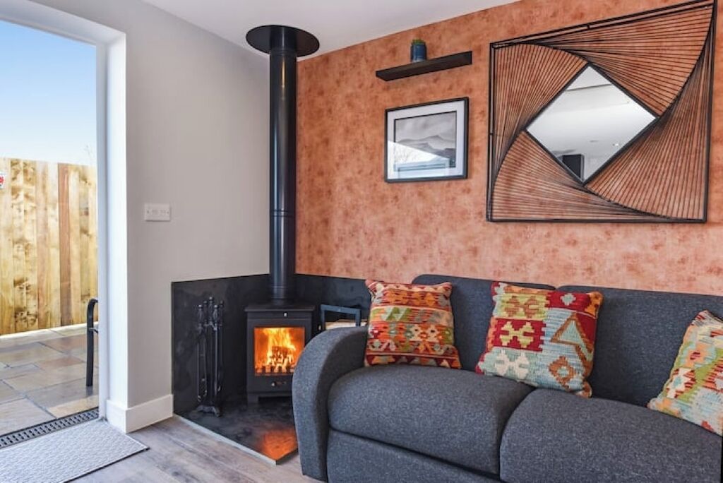 A cozy living room with a fireplace, a sofa with patterned cushions, and a wall-mounted mirror.