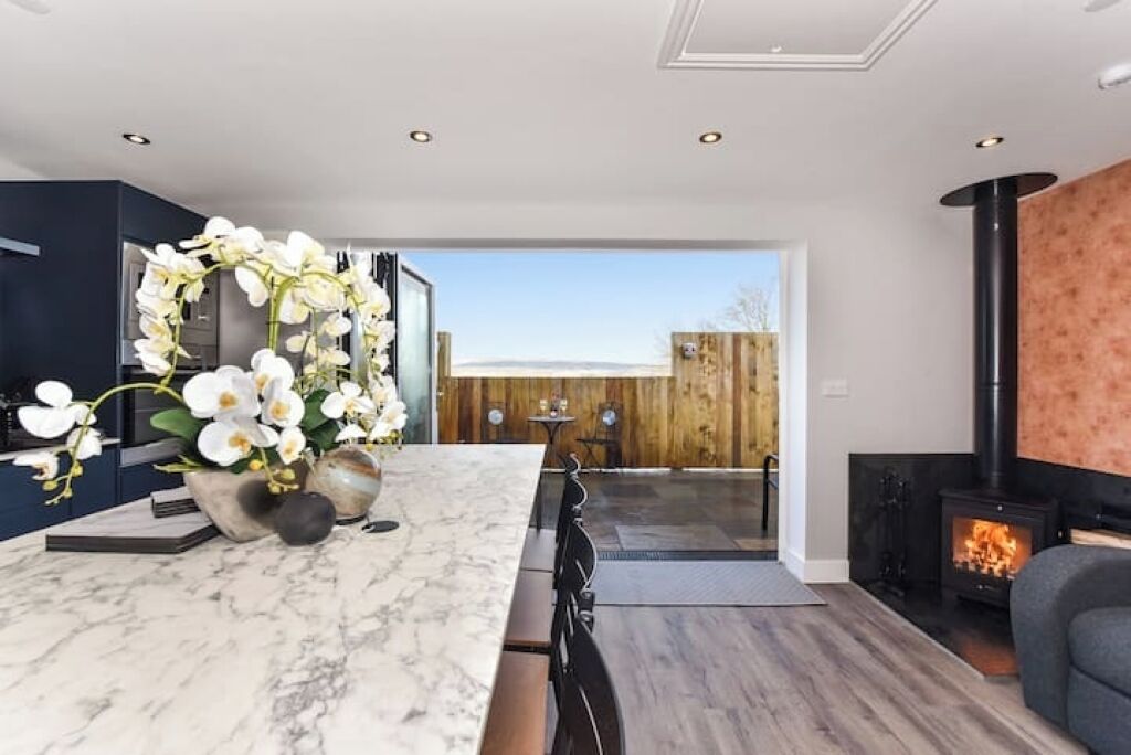 A modern kitchen with a marble countertop, a large white orchid arrangement, and a wood-burning stove.