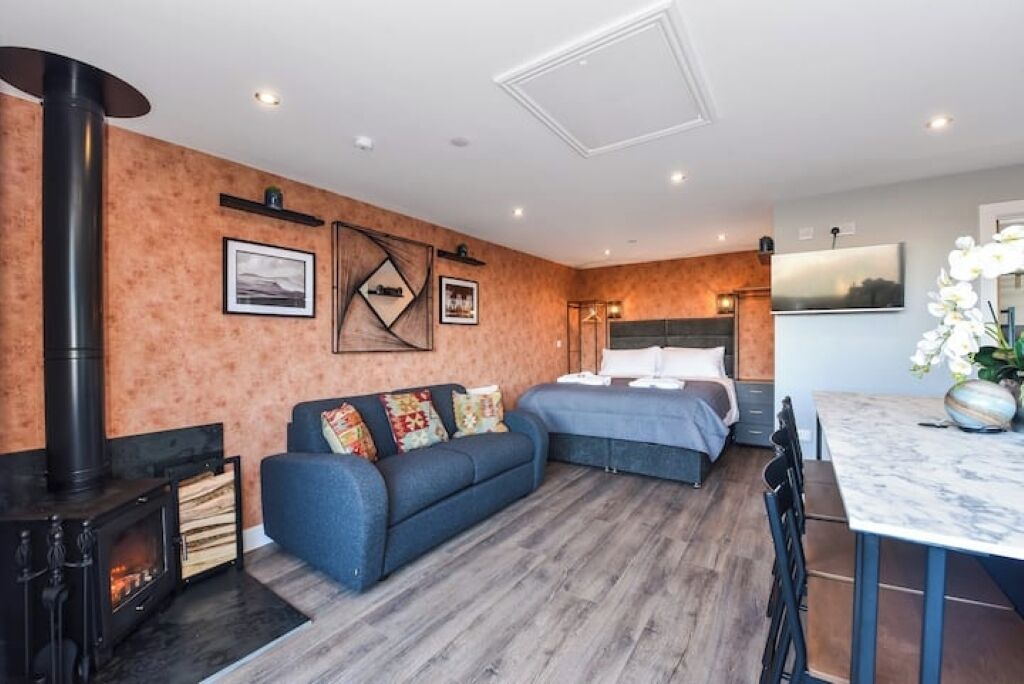 A cozy room with a sofa, a bed, a dining table, and a fireplace.