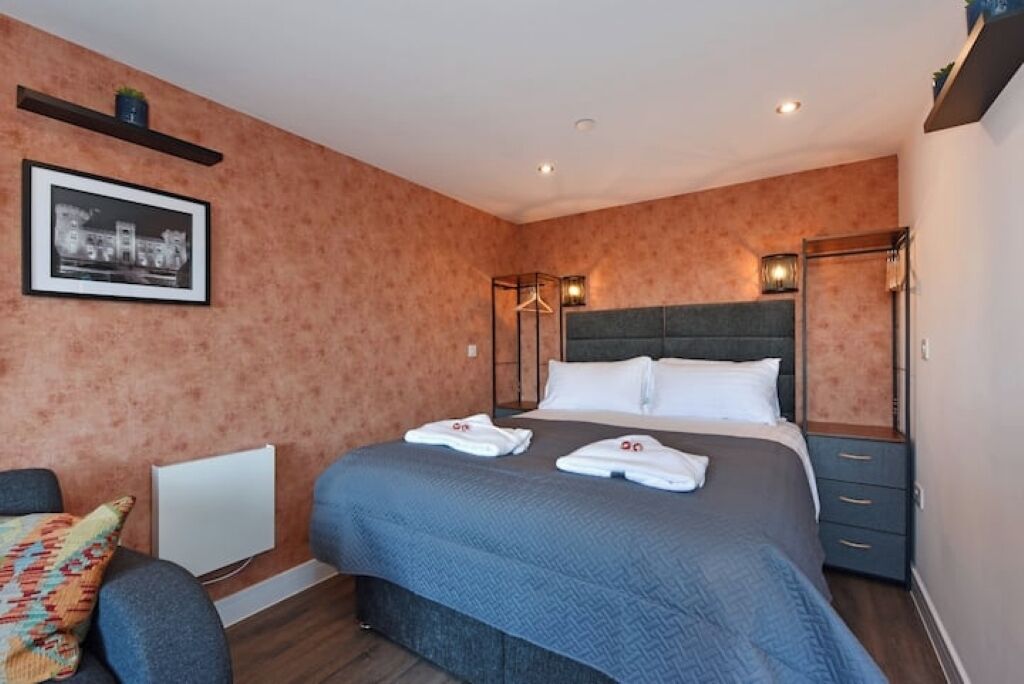A neatly arranged hotel room with a large bed, a bedside table, a chair, and a wardrobe.