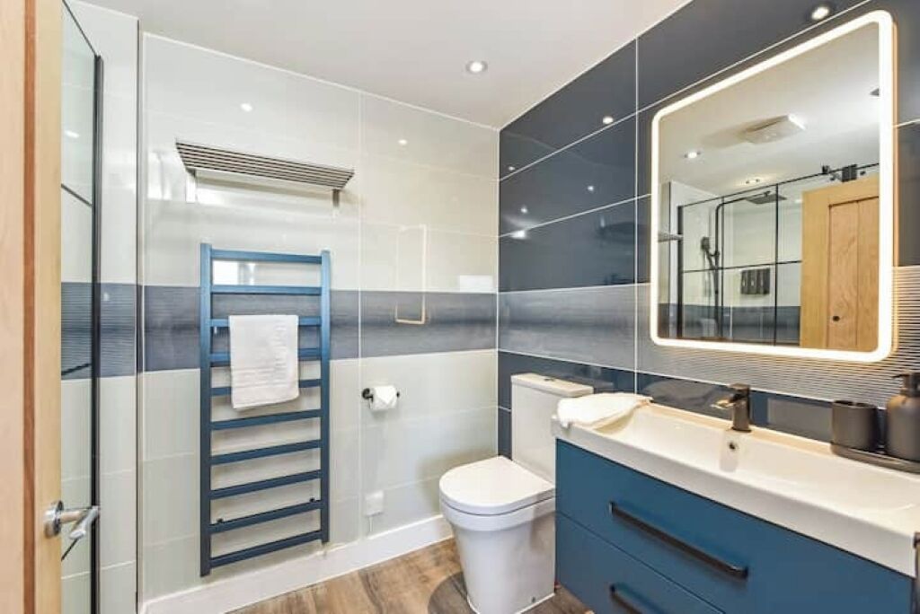 Ein modernes Badezimmer mit Duschkabine aus Glas, einer weißen Toilette, einem blauen Waschtisch mit Spiegel und einem Handtuchhalter.
