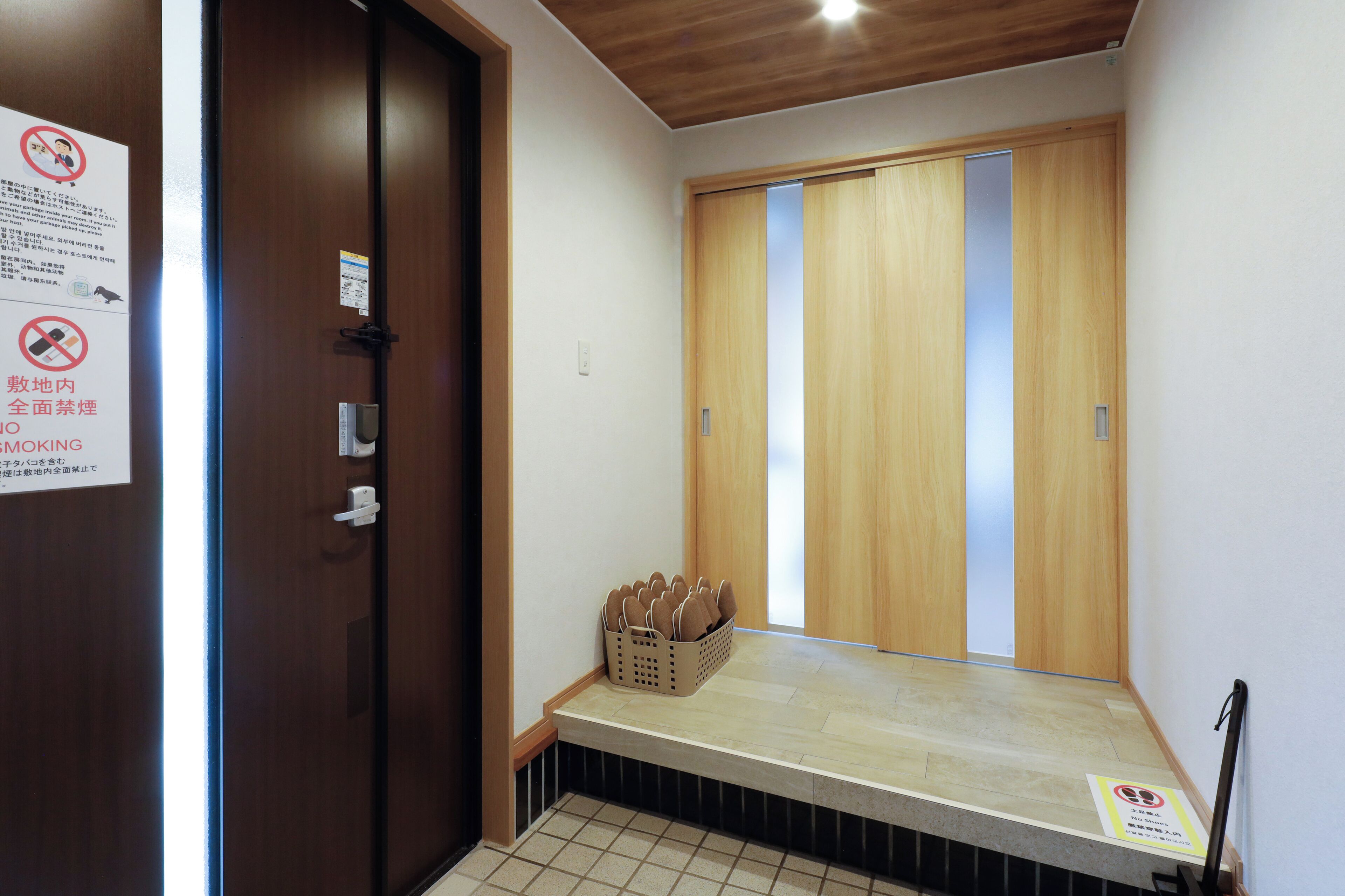 Habitación de hotel con puerta de madera, un pequeño banco y un cesto de pantuflas.