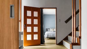 A hallway leading to a bedroom with a wooden door, a staircase, and a bed with a white duvet. - THE VILLA SEASIDE (Abashiri)