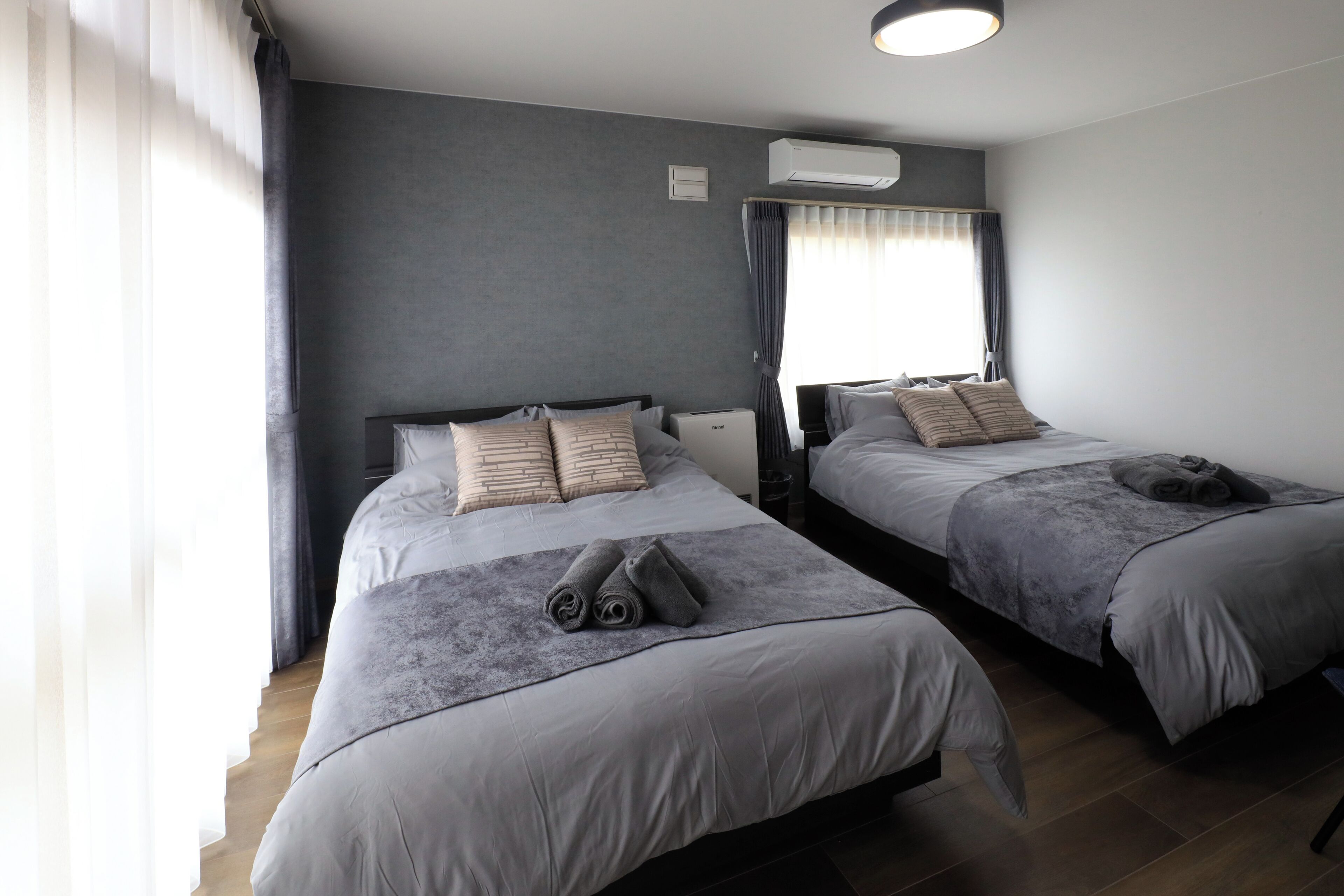 Habitación de hotel con dos camas, ropa de cama gris, alfombra gris y una ventana con cortinas.