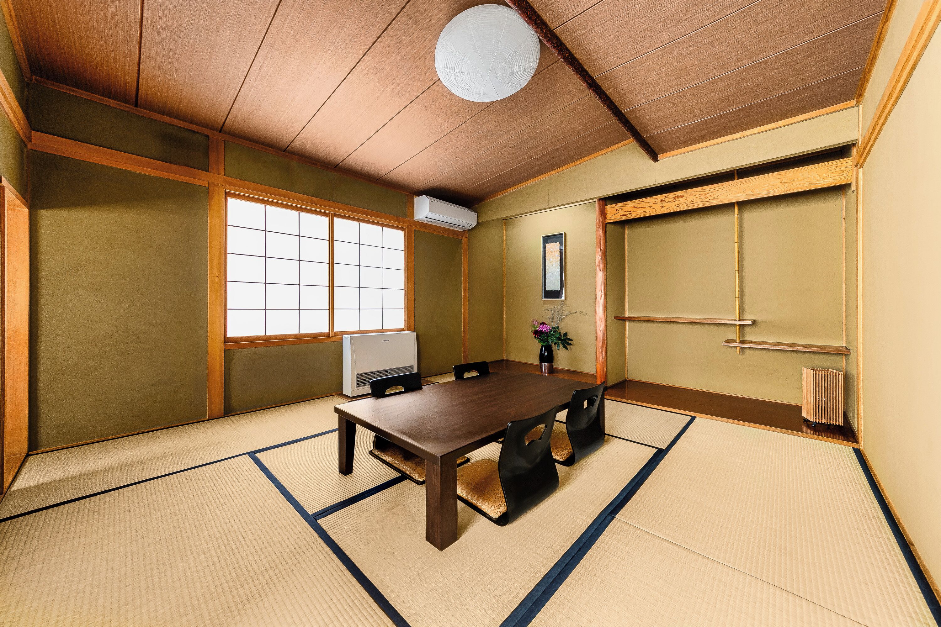 Ein traditioneller japanischer Raum mit Tatami-Böden, einem Holztisch, Tatami-Matten, einem Fenster und einer wandmontierten Klimaanlage.