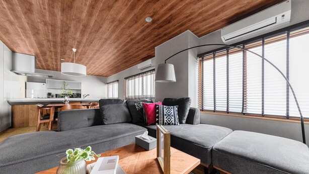 A modern living room with a wooden ceiling, grey sofas, a wooden coffee table, and a kitchen in the background. - THE VILLA SEASIDE (Abashiri)
