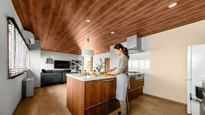 A modern kitchen with wooden cabinetry, a central island, and a built-in oven. - THE VILLA SEASIDE (Abashiri)