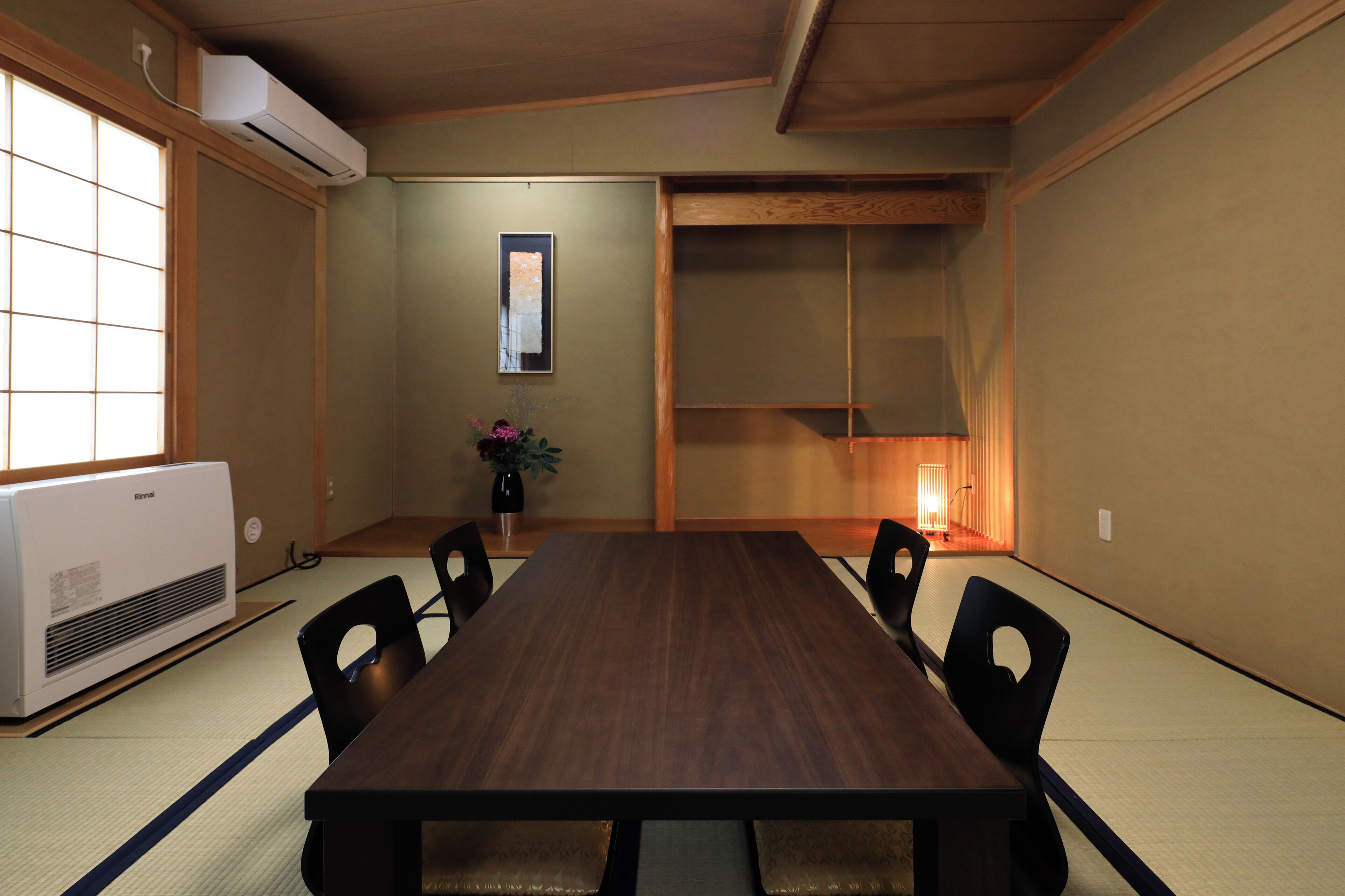 A traditional Japanese room with tatami flooring, a wooden table, and black chairs.