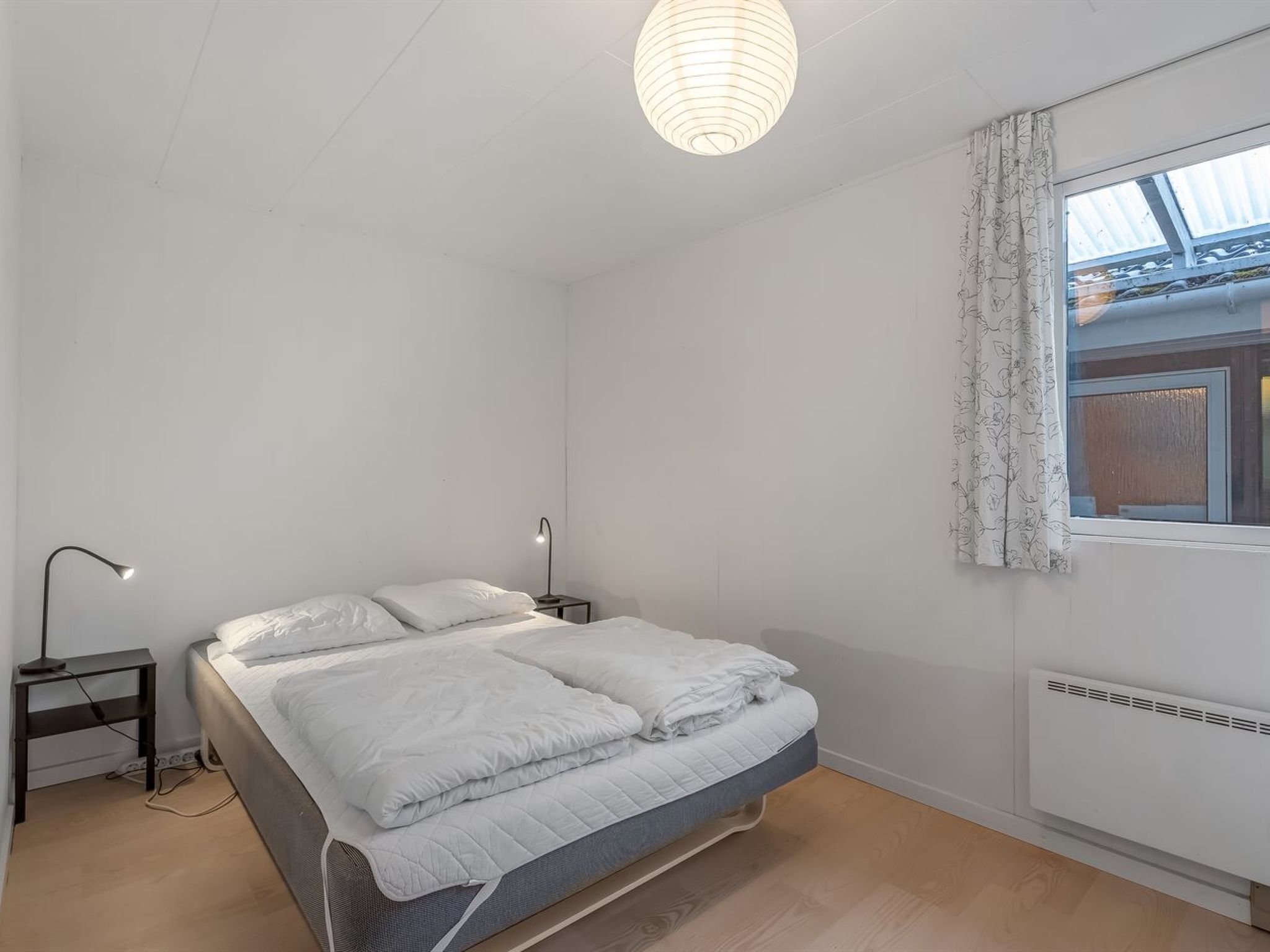 Un dormitorio con cama, lámparas de noche, una ventana con cortinas y un candelabro en el techo.