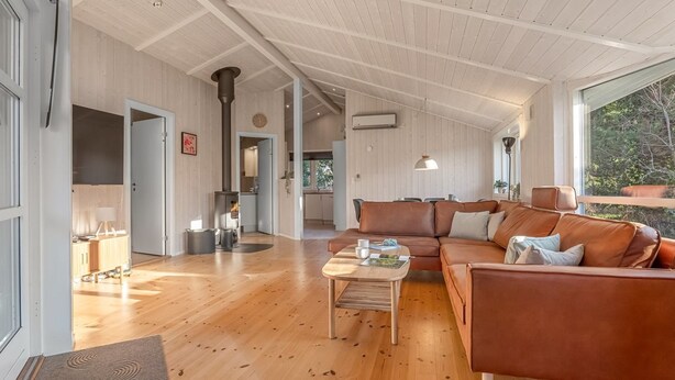 A spacious living area with a wooden floor, a brown leather sofa, a coffee table, and a large window offering a view of the outdoors. - "Nashota" - 600m from the sea by Interhome (V æggerløse)