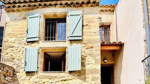 A stone building with a central archway, wooden shutters, and a staircase leading to an upper level.