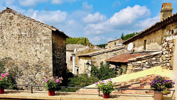 Two wicker chairs on a tiled patio with stone buildings in the background.