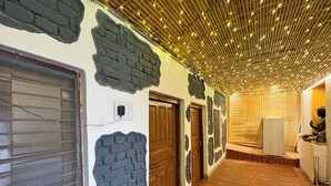 Un couloir avec un mur en briques apparentes, des portes en bois et un plafond décoré de guirlandes lumineuses.