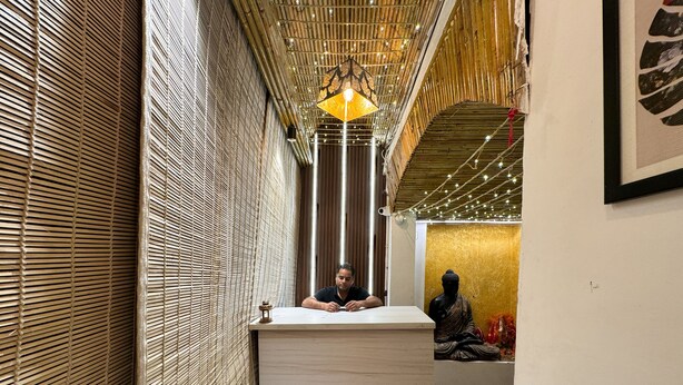 Un espace d’accueil avec un mur en bambou, un comptoir de réception en bois, un luminaire suspendu et une statue de Bouddha en arrière-plan.