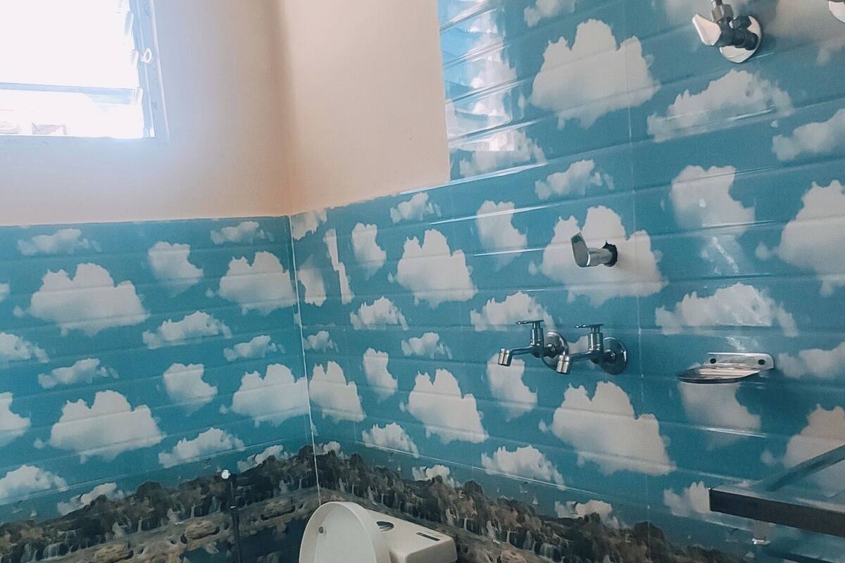 Un baño con inodoro, lavamanos y ducha. Las paredes están decoradas con un diseño de nubes.