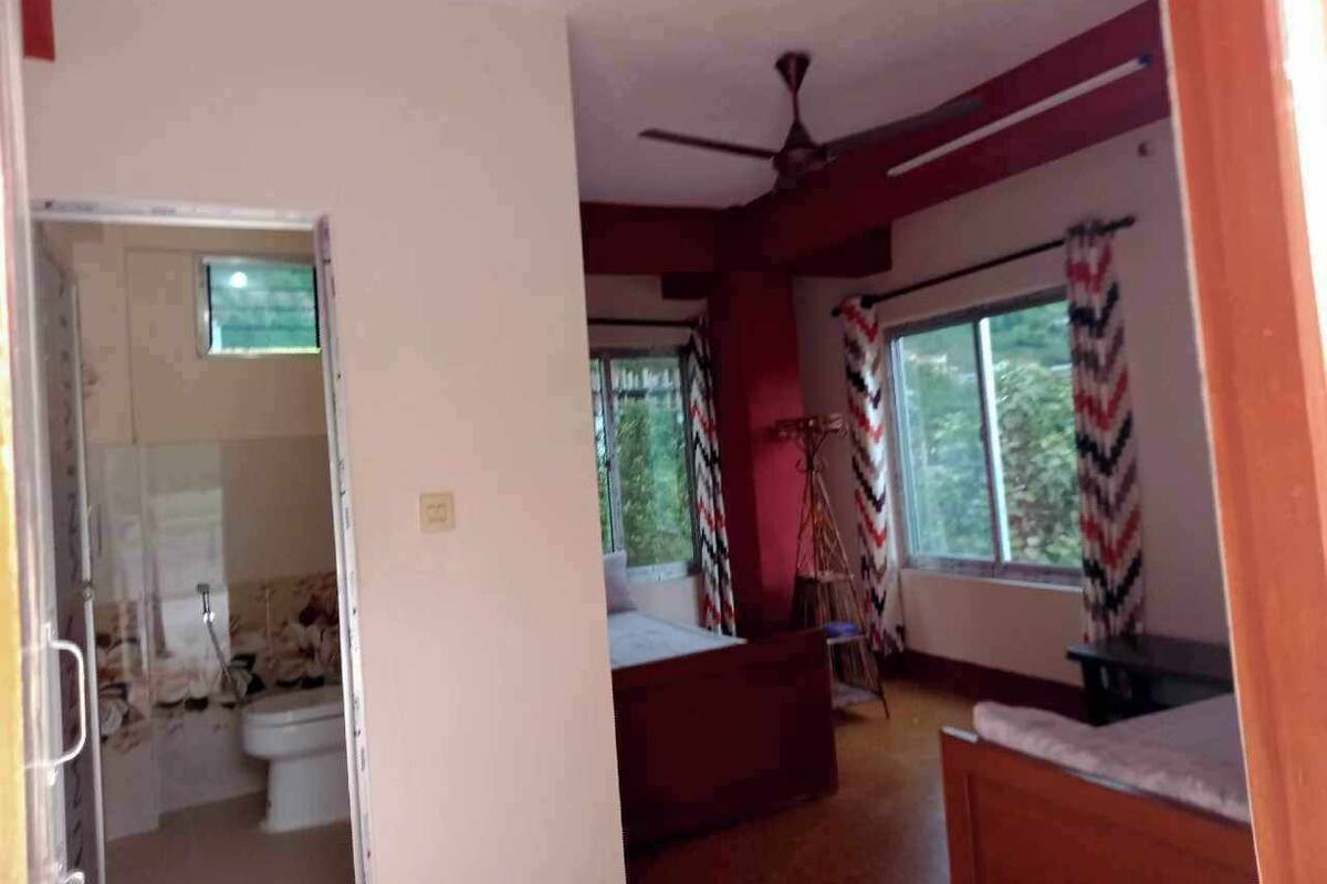 Una habitación con cama, ventilador de techo, ventana con cortinas y vista al exterior.