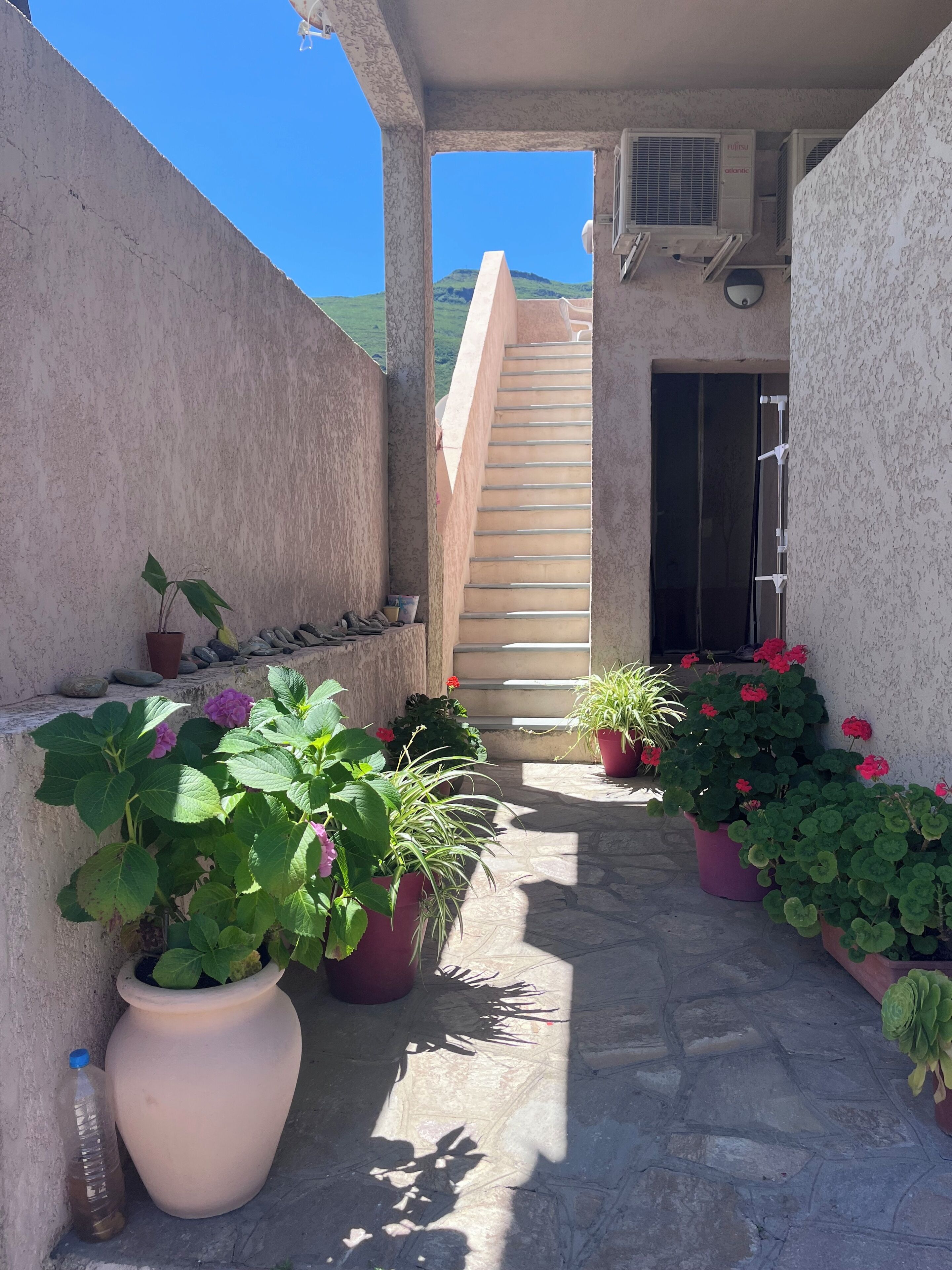 Un espacio al aire libre con pavimento de piedra, plantas en macetas, una escalera y un equipo de aire acondicionado.