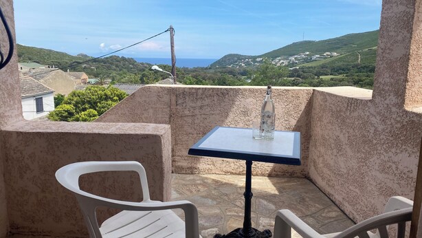 Un balcon avec une table et deux chaises, offrant une vue panoramique sur un paysage vallonné et un ciel dégagé.