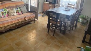 Un salon avec un canapé, une table à manger avec des chaises, et un coin cuisine visible à travers une porte ouverte.