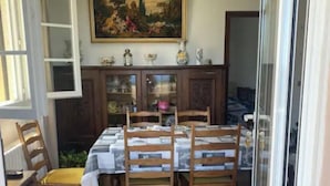 Un coin repas avec une table dressée pour quatre personnes, des chaises en bois, un buffet aux portes vitrées et un tableau accroché au-dessus de la table.