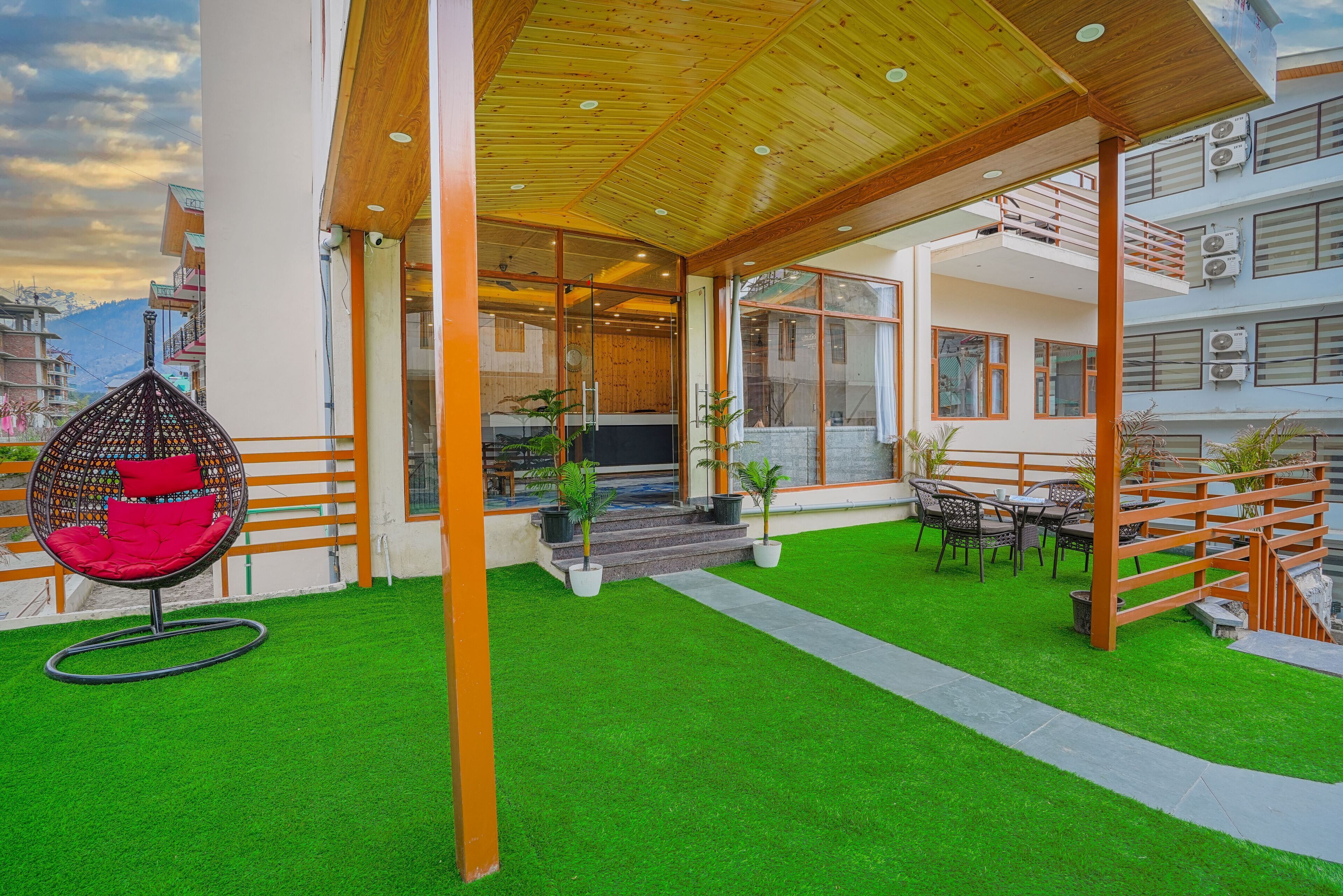 A modern outdoor patio with artificial grass, a hanging chair, and a dining area with tables and chairs.