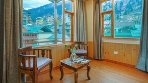 A room with wooden walls and floors, two wooden chairs, a wooden table with a vase and pictures, and large windows with curtains. - Hotel Divine Paradise Manali (Manali)