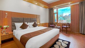 A wooden-paneled bedroom with a large bed, a nightstand, a desk, and a view of the outdoors. - Hotel Divine Paradise Manali (Manali)