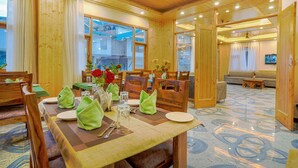A wooden dining area with a table set for four, chairs, and a view of the outside. - Hotel Divine Paradise Manali (Manali)