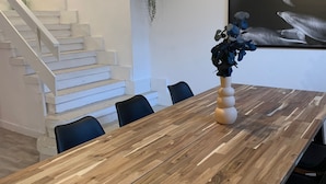 Ein Essbereich mit Holztisch, Stühlen, einer Vase mit Blumen, einer Pendelleuchte und einer Treppe mit Pflanze.
