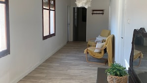 Ein Flur mit Holzboden, einem Sessel mit gelber Sitzfläche, einem Blumentopf und einer Pendelleuchte.
