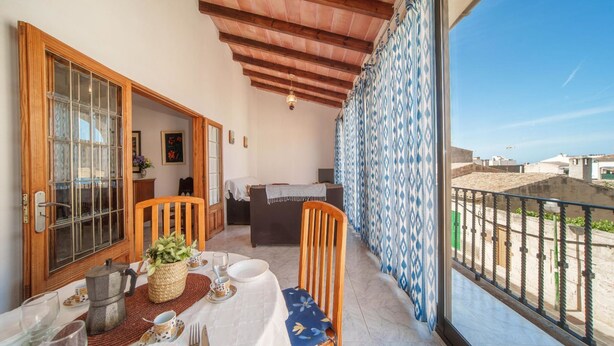 Een balkon met een eettafel, een houten stoel en uitzicht op de omgeving.