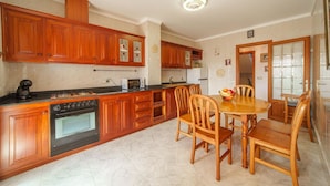 Een keuken met houten kastjes, een fornuis en een eettafel met stoelen.