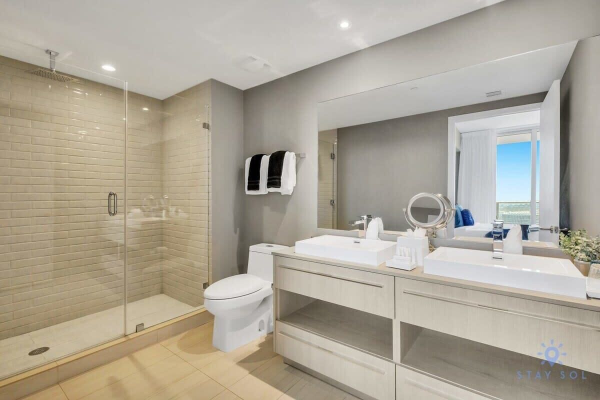 A modern bathroom with a glass-enclosed shower, a white toilet, and a vanity with a large mirror.