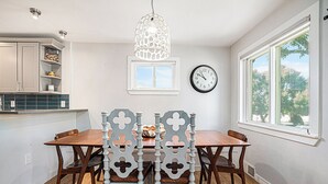 A dining area with a wooden table and chairs, a hanging light fixture, a clock, and a window with a view of trees. - Backyard Wonderland: Ultimate Outdoor Fun (Denver)