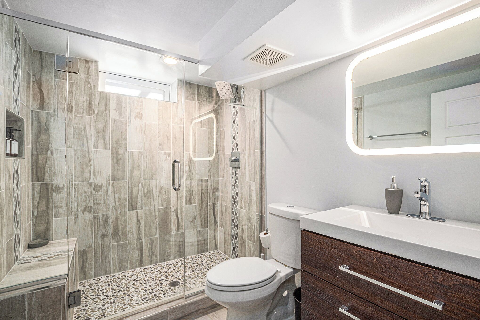 A modern bathroom with a glass-enclosed shower, a white toilet, and a vanity with a mirror.