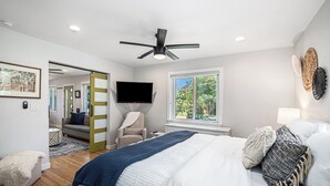 A bedroom with a bed, a ceiling fan, a TV, a window, and a chair. - Backyard Wonderland: Ultimate Outdoor Fun (Denver)